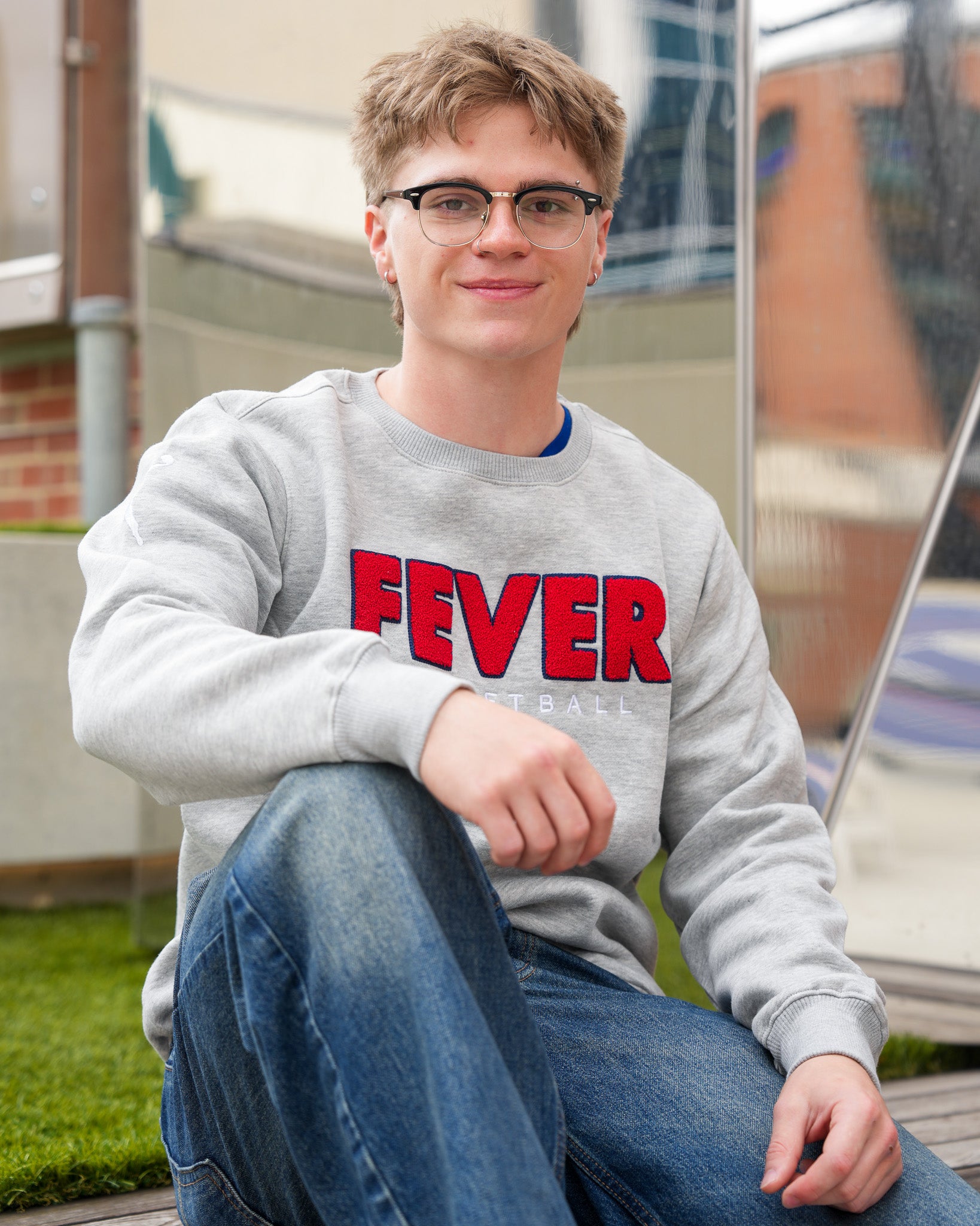 Person wearing a gray sweatshirt with 'FEVER' printed on it, sitting outdoors.