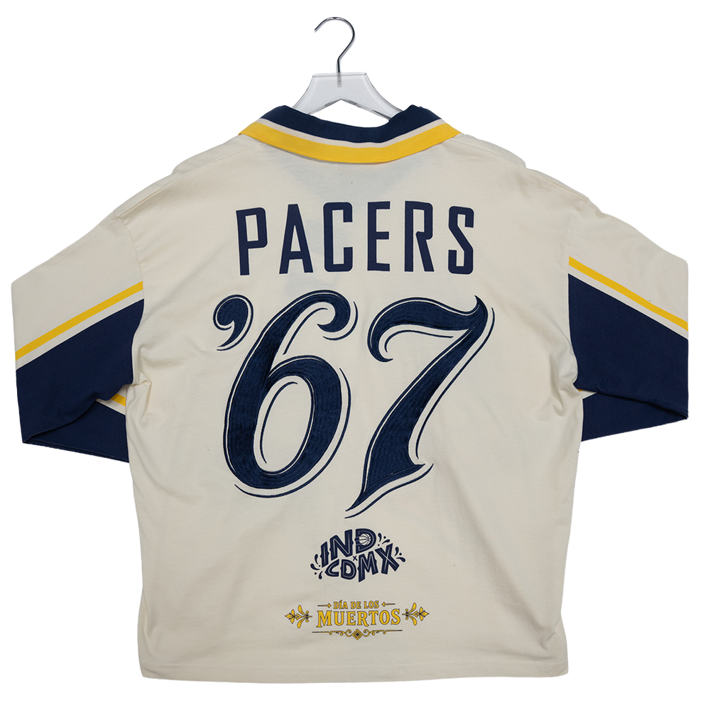 Back view of a cream-colored sports jersey hanging on a hanger, featuring navy blue and yellow accents, the word 'PACERS', large number '67', and 'IND COMK' and 'Los Altos Musertos' graphics.
