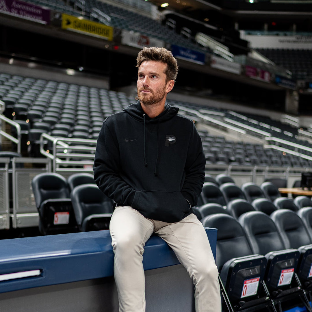 Man sitting on a blue bench in an indoor sports arena with empty seats.