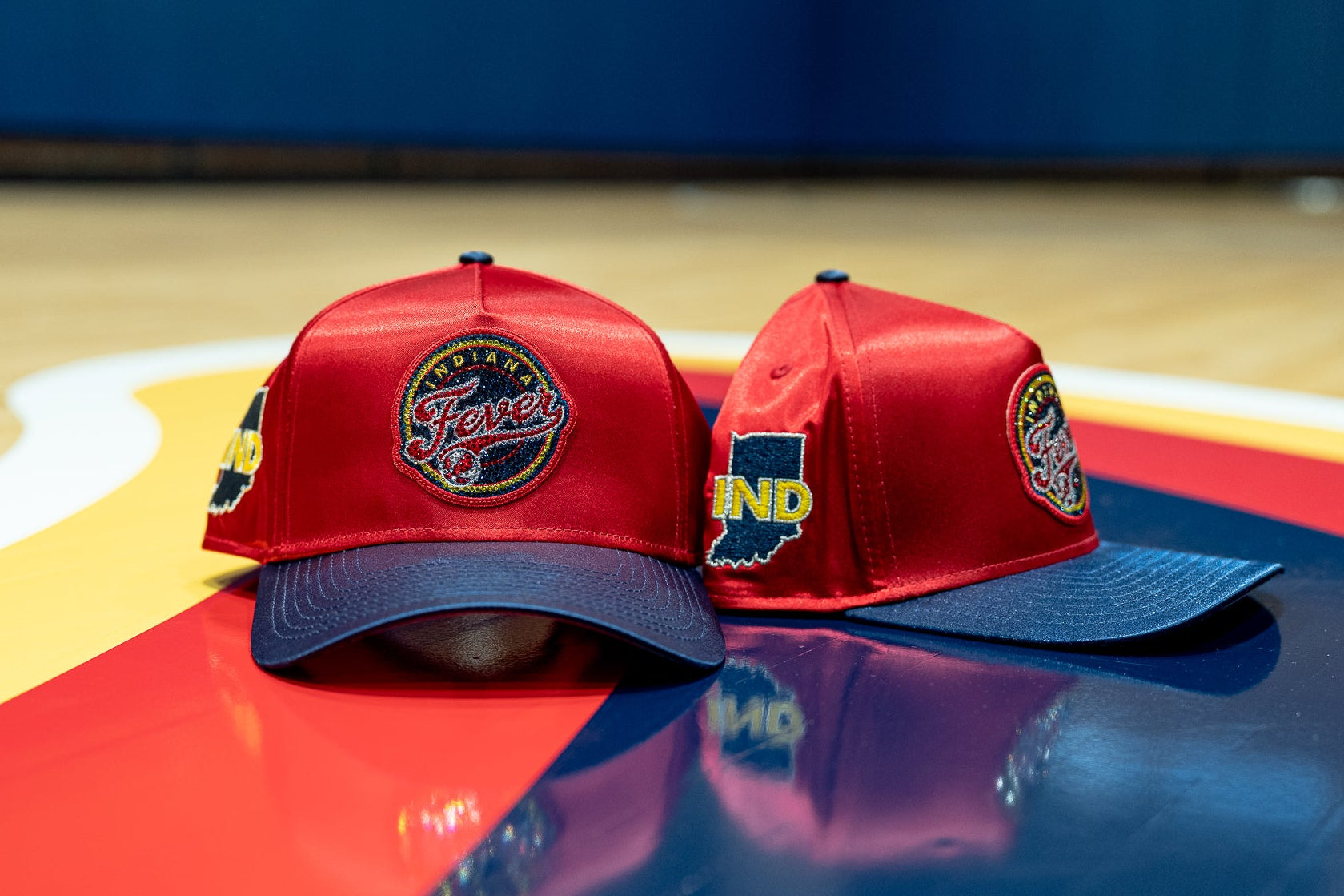 Two red baseball caps with blue visors on a sports court surface.