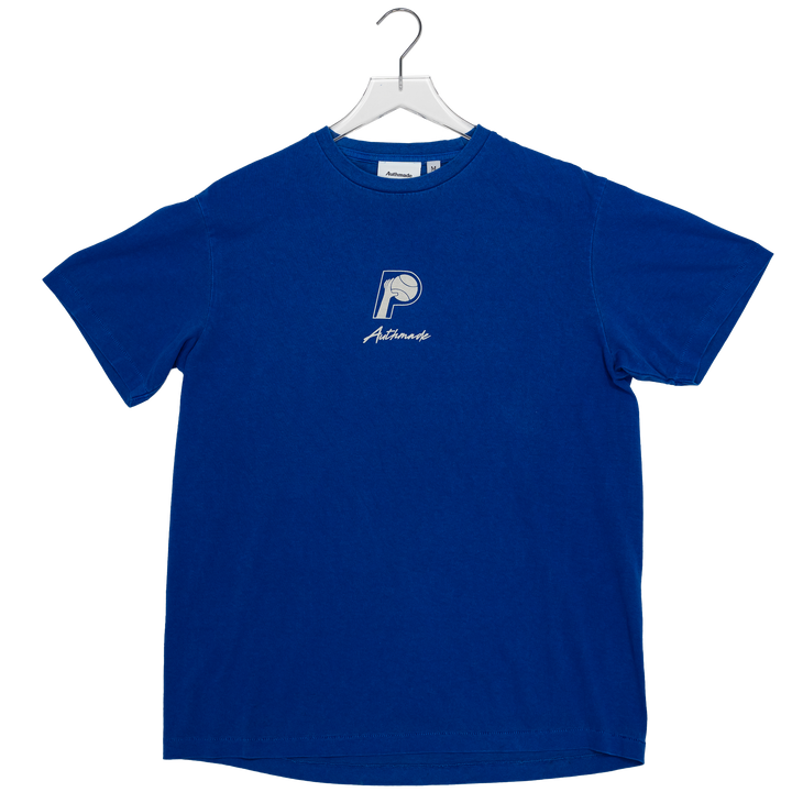 A royal blue short-sleeve t-shirt hanging on a white hanger against a plain white background. The shirt features a small white embroidered logo on the left chest with a basketball graphic and the word &