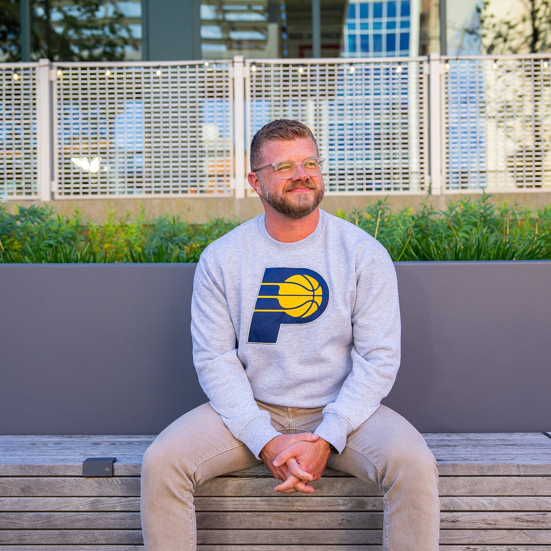 Man sitting on a bench wearing a gray sweatshirt with a logo, outdoors.