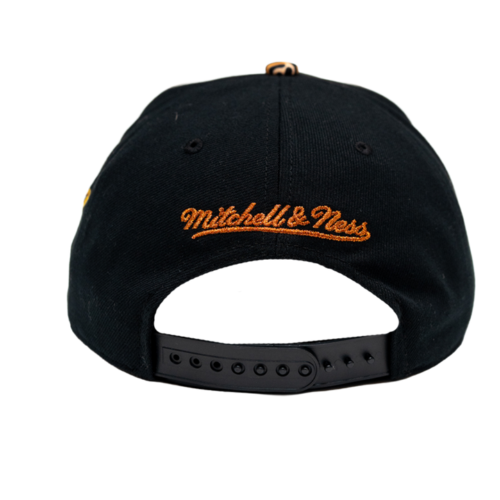 The back of a black Mitchell & Ness baseball cap with orange embroidered script logo and a black adjustable snapback strap.