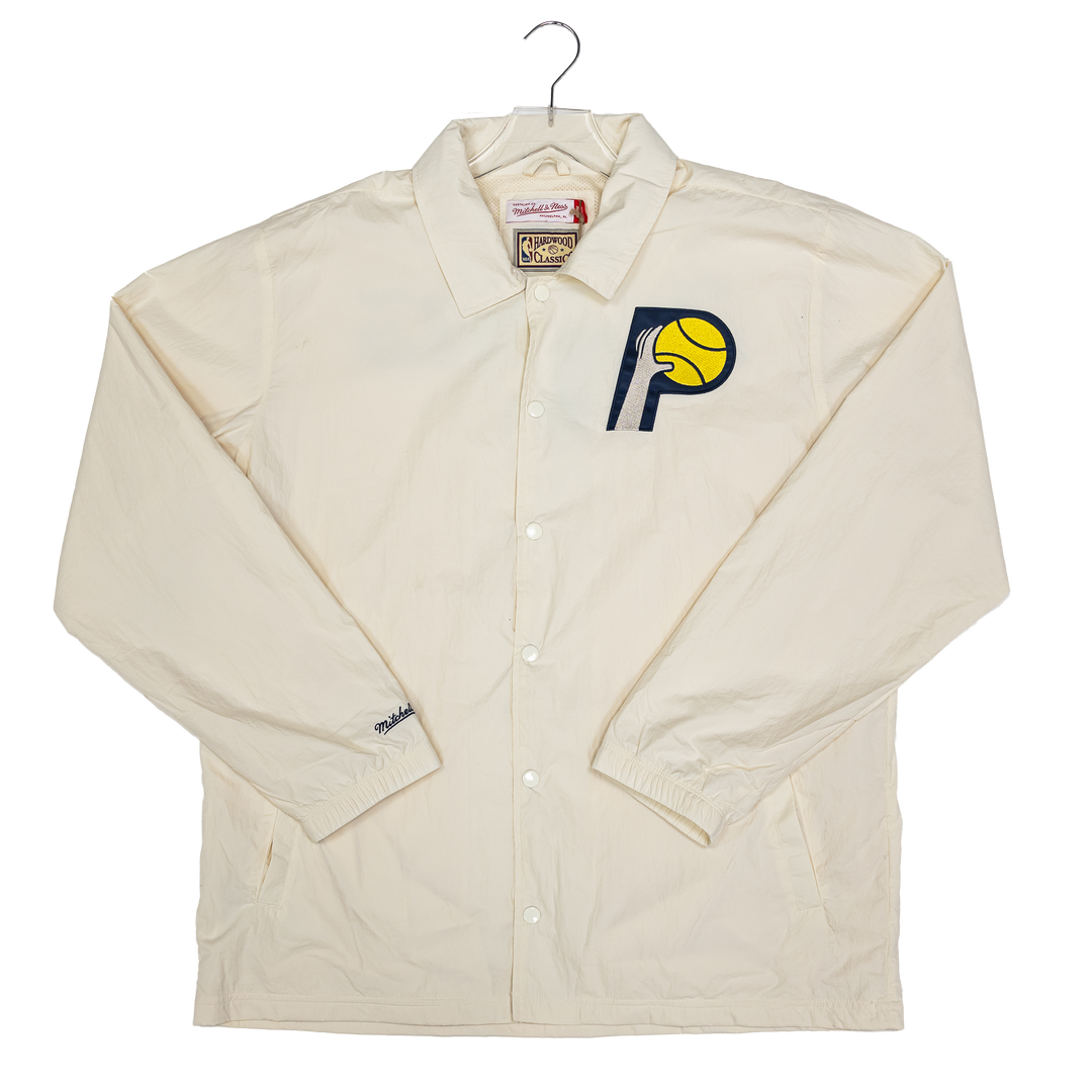 An off-white/cream long-sleeve button-up coach jacket from Mitchell &amp; Ness, displayed on a hanger against a white background. It features the Indiana Pacers logo embroidered on the left chest.